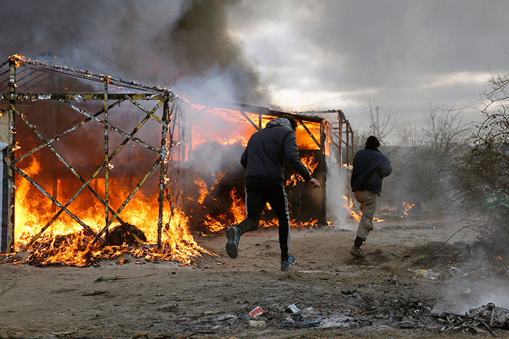 Migrants run past burning tents in a makeshift camp near Calais, France, Monday Feb. 29, 2016. French authorities have begun dismantling part of the sprawling camp locally referred to as "the jungle" where thousands are hanging out, hoping to make their way to a better life in Britain. 