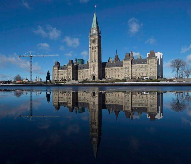 The centre block of the Parliament buildings is reflected in a puddle as a woman walks past, in Ottawa on February 1, 2016.  (File photo).
