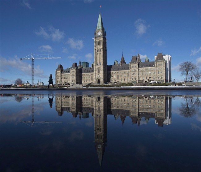 The centre block of the Parliament buildings is reflected in a puddle as a woman walks past, in Ottawa on February 1, 2016.  (File photo).