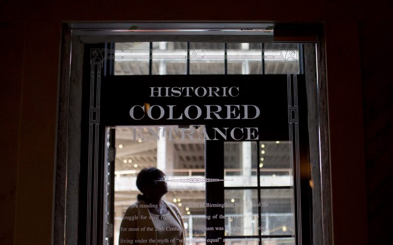 In this Thursday, Jan. 7, 2016 photo, a woman stands in the doorway of then new Historic Colored Entrance at the Lyric Theatre, in Birmingham, Ala. 