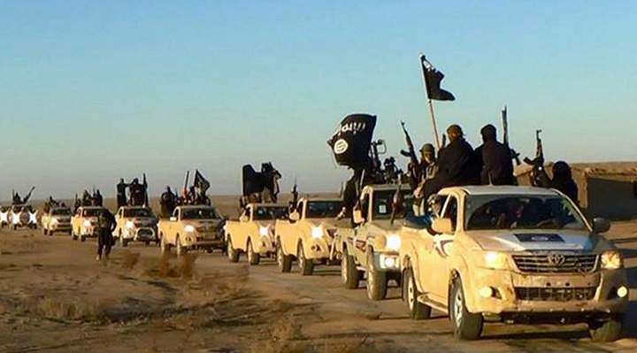 Militants of the Islamic State group hold up their weapons and wave its flags on their vehicles in a convoy on a road leading to Iraq, in Raqqa, Syria. 