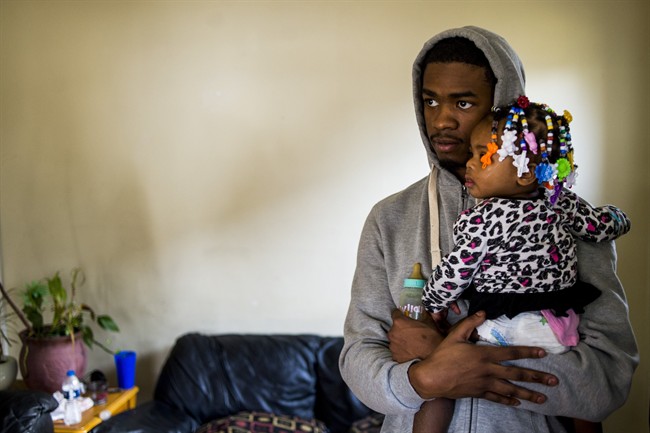 Dwight "DJ" Earnest, 23, holds his 1-year-old daughter Zariah Cade in his home on the west side of Flint, Mich., on Monday, Feb. 1, 2016.
