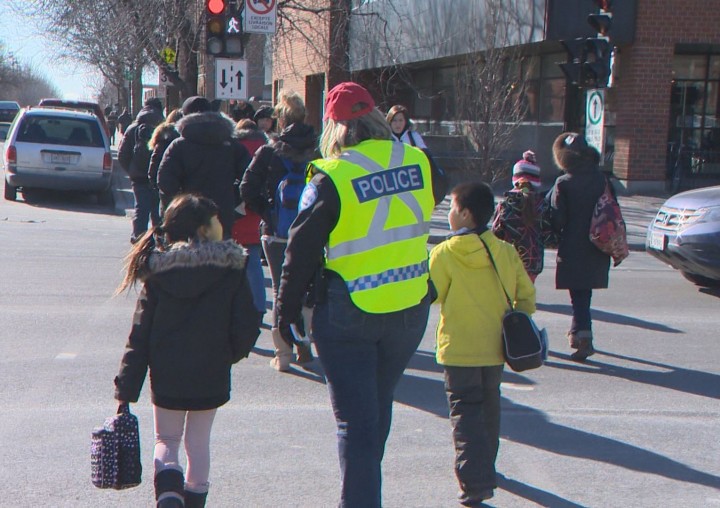 A Montreal police officer escorts children across a busy intersection to promote pedestrian safety, Tuesday, February 2, 2016.