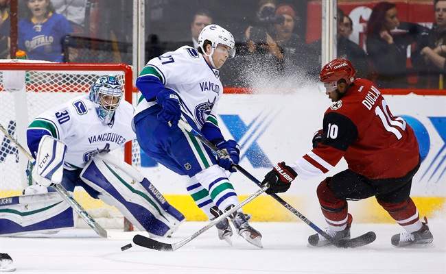 Arizona Coyotes' Anthony Duclair (10) tries to get off a shot past Vancouver Canucks' Ben Hutton (27) as Canucks' goalie Ryan Miller (30) gets in position for the save during the first period of an NHL hockey game Wednesday, Feb. 10, 2016, in Glendale, Ariz.