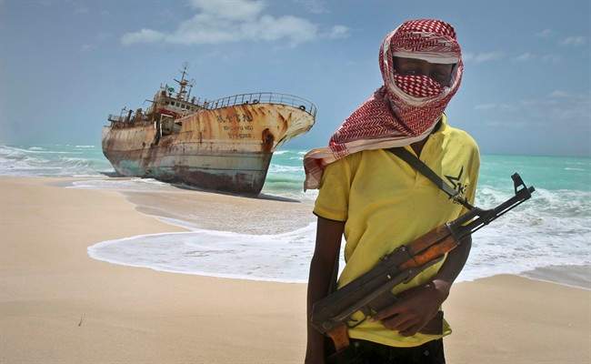 In this Sept. 23, 2012 file photo, masked Somali pirate Hassan stands near a Taiwanese fishing vessel that washed up on shore after the pirates were paid a ransom and released the crew, in the once-bustling pirate den of Hobyo, Somalia. 