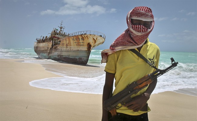 In this Sept. 23, 2012 file photo, masked Somali pirate Hassan stands near a Taiwanese fishing vessel that washed up on shore after the pirates were paid a ransom and released the crew, in the once-bustling pirate den of Hobyo, Somalia. 