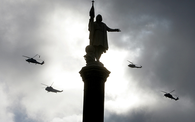 Helicopters fly past a statue of Columbus, in Madrid.