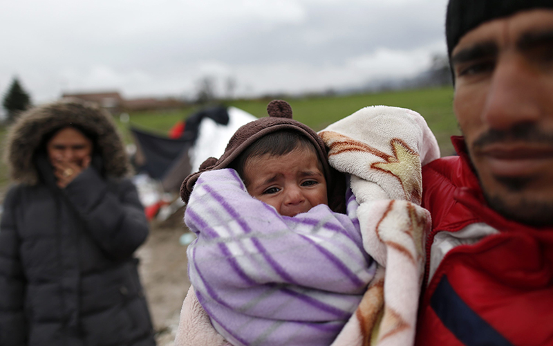 Yousif Shikhmous, a migrant from Syria holding his baby named Merkkel in an improvised camp on the border line between Macedonia and Serbia near the northern Macedonian village of Tabanovce, Friday, March 11, 2016.  