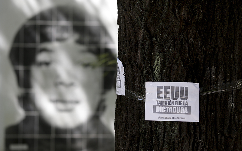 A picture of a person that was disappeared during the last military dictatorship, is seen behind a leaflet on a tree that reads in Spanish "The U.S. was also the dictatorship, Obama out of former Argentine Navy School of Mechanics" in Buenos Aires, Argentina, Wednesday, March 16, 2016. 