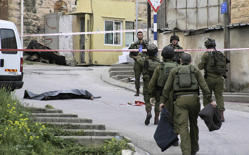 Israeli soldiers stand near the body of a Palestinian who was shot and killed by a soldier while laying wounded on the ground after an attack in Hebron, West Bank.  