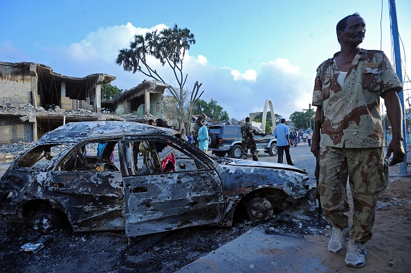 Somali soldiers and resident stand near wreckage car and buildings on February 27, 2016, in Mogadishu, Somalia.
