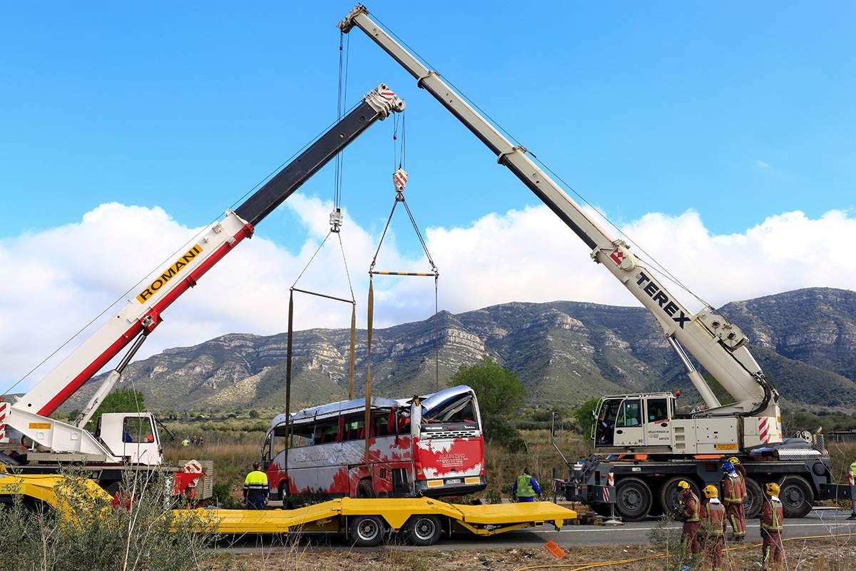 Emergency personnel look on as two cranes hoist a bus onto a trailer on the Spanish AP-7 motorway near Freginals, Amposta south of Tarragona following a fatal accident that claimed the lives of 13 foreign students an injured 44 others early on March 20, 2016.