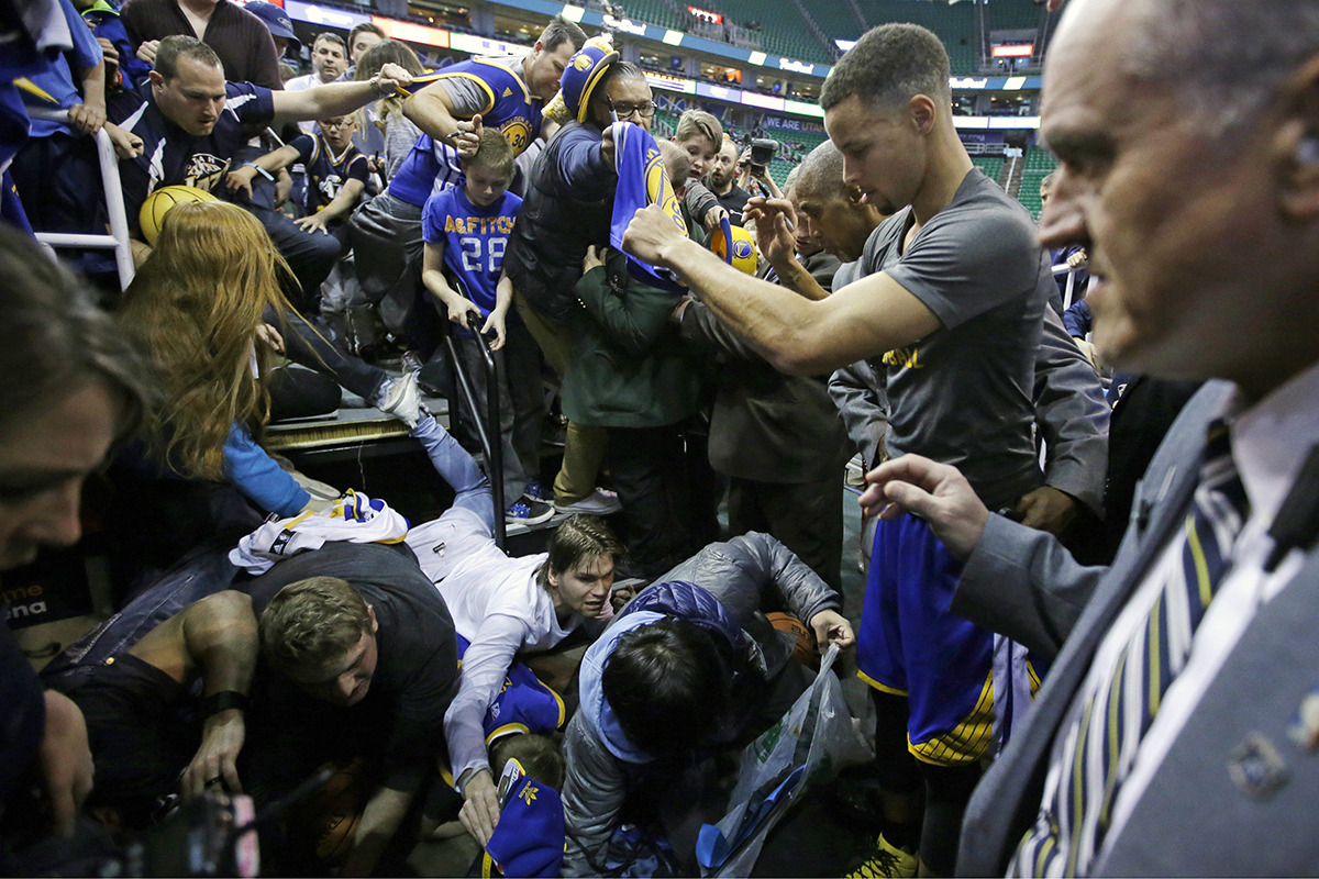 Golden State Warriors guard Stephen Curry, right, watches as fans fall from the stands after a railing broke, while he signs autographs before the start of their game with the Utah Jazz.