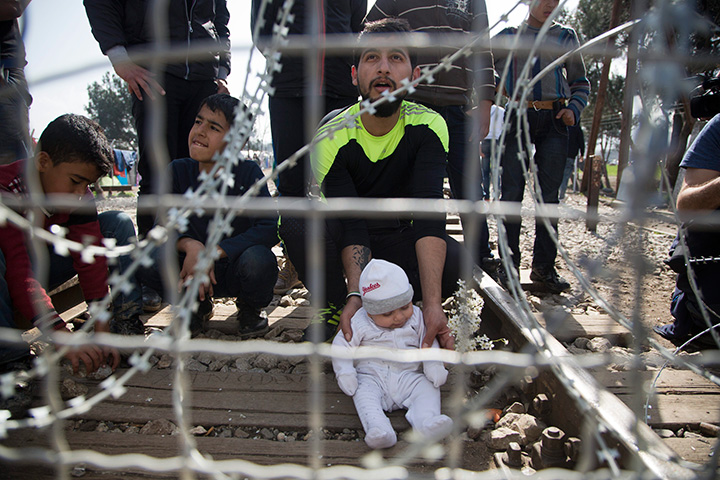 A migrant father with his child waits on the Greek side of the border to enter Macedonia near the southern Macedonian town of Gevgelija, Tuesday, March 1, 2016.  