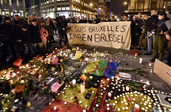 People holding a banner reading "I am Brussels" behind flowers and candles to mourn for the victims at Place de la Bourse in the center of Brussels, Tuesday, March 22, 2016.