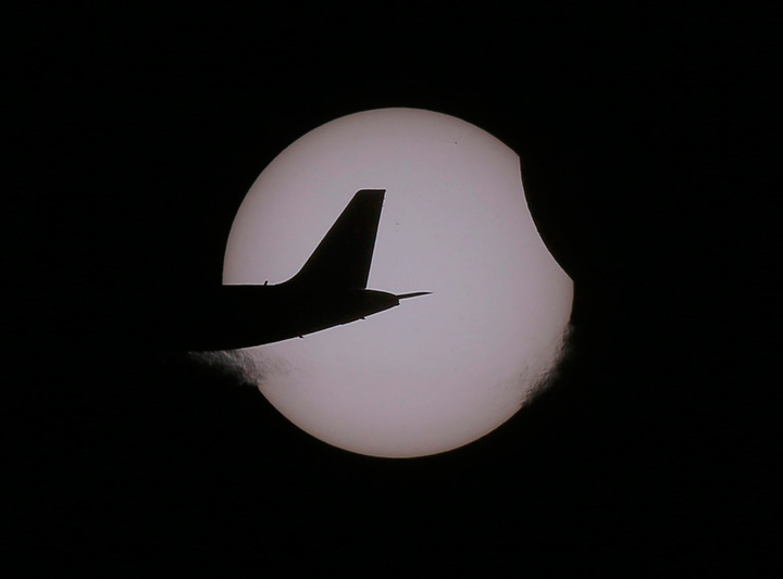 An Air Asia passenger plane flies as a partial solar eclipse occurs Wednesday, March 9, 2016 as seen from Taguig city, east of Manila, Philippines.