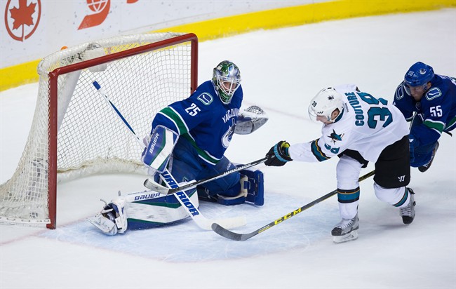 San Jose Sharks' Logan Couture, second right, scores against Vancouver Canucks' goalie Jacob Markstrom, of Sweden, while being checked by Alex Biega during the second period of an NHL hockey game in Vancouver, B.C., on Tuesday March 29, 2016.
