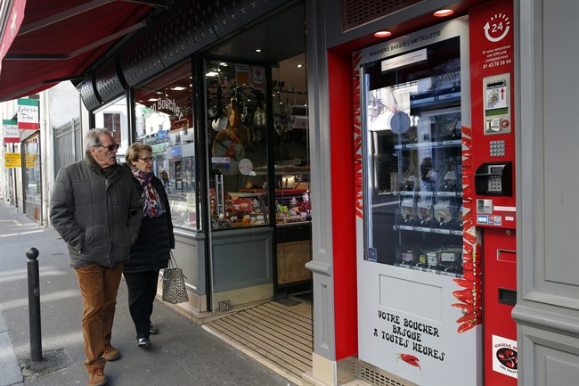 Residents watch the first meat vending machine installed in the French capital, in Paris, Tuesday, March 15, 2016. With their beloved baguette already available 24 hours a day, it seems only logical that Parisians can now get the Bayonne ham and Basque pate that goes so well with it from the first meat vending machine installed in the French capital.
