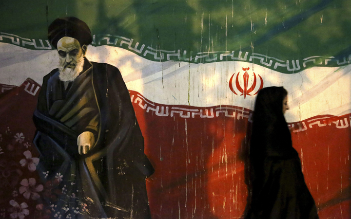A veiled Iranian woman walks past a mural depicting the late revolutionary founder Ayatollah Khomeini, and national Iranian flag, painted on the wall of the former U.S. Embassy, in Tehran, Iran. 