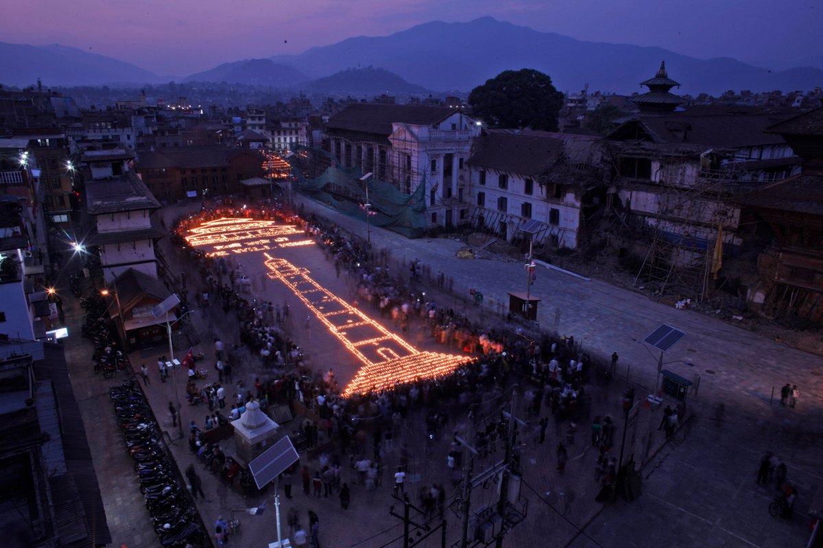 Nepalese people light up candles in the shape of the Dharahara Tower, center and the Kasthamandap temple, top left, which were destroyed in last year's devastating earthquake at the Basantapur Durbar Square in Kathmandu, Nepal, Sunday, April 24, 2016. Nepalese held memorial services to mark the anniversary of the disaster that killed nearly 9,000 people and left millions homeless. 