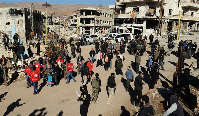 In this file photo released on December 28, 2015, by the Syrian official news agency SANA, Syrian opposition fighters and their families gather at a square surrounded by damaged buildings, as they prepare to evacuate the town of Zabadani, in Syria. A young man has died of malnutrition and a surgeon killed by a sniper in two besieged towns in western Syria this past month is a stark reminder that sieges continue to kill Syrians despite international efforts to defuse them in halting negotiations in Europe. 