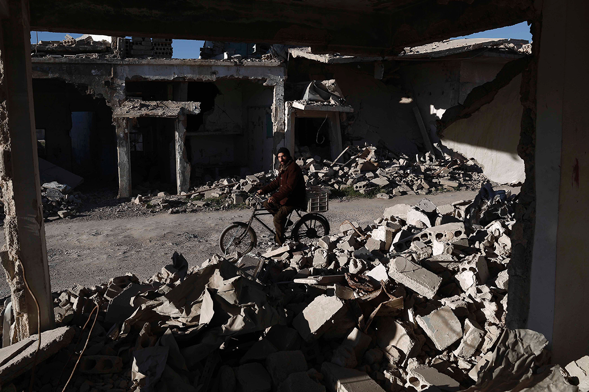 A Syrian man rides his bicycle past the rubble of destroyed buildings on March 7, 2016, in the rebel-held town of Douma, on the outskirts of the capital Damascus. 