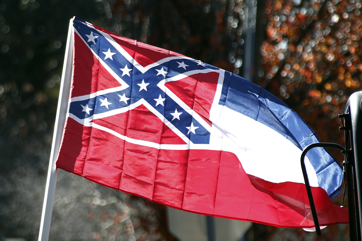 In this Tuesday, Jan. 19, 2016 photo, a state flag of Mississippi is unfurled by Sons of Confederate Veterans and other groups on the grounds of the state Capitol in Jackson, Miss., in support of keeping the Confederate battle emblem on the state flag.