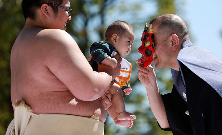 A referee puts an ogre mask to make a baby, who is held by a college sumo wrestler, cry to win in the crying baby contest at Sensoji Buddhist temple in Tokyo, Friday, April 29, 2016.