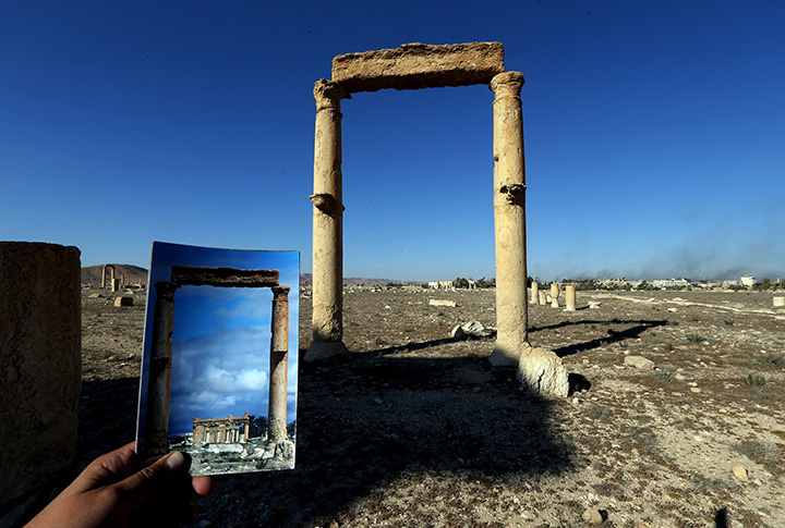 A picture taken on March 31, 2016 shows a photographer holding his picture of the Temple of Baal Shamin seen through two Corinthian columns on March 14, 2014 in front of the remains of the historic in the ancient Syrian city of Palmyra.