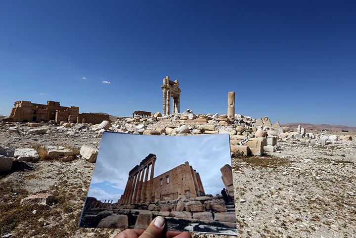 A general view taken on March 31, 2016 shows a photographer holding his picture of the Temple of Bel taken on March 14, 2014 in front of the remains of the historic temple in the ancient Syrian city of Palmyra.