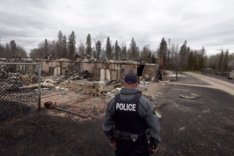 A police officer looks over a fire-damged building in the Abasands neighbourhood in Fort McMurray, Alta., Monday, May 9.