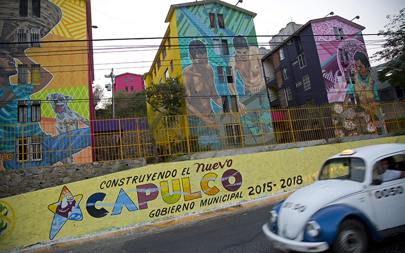 A taxi drives past the Cuauhtemoc Housing Unit and a municipal sign with a message that reads in Spanish; "Building the new Acapulco" in Acapulco, Mexico. 