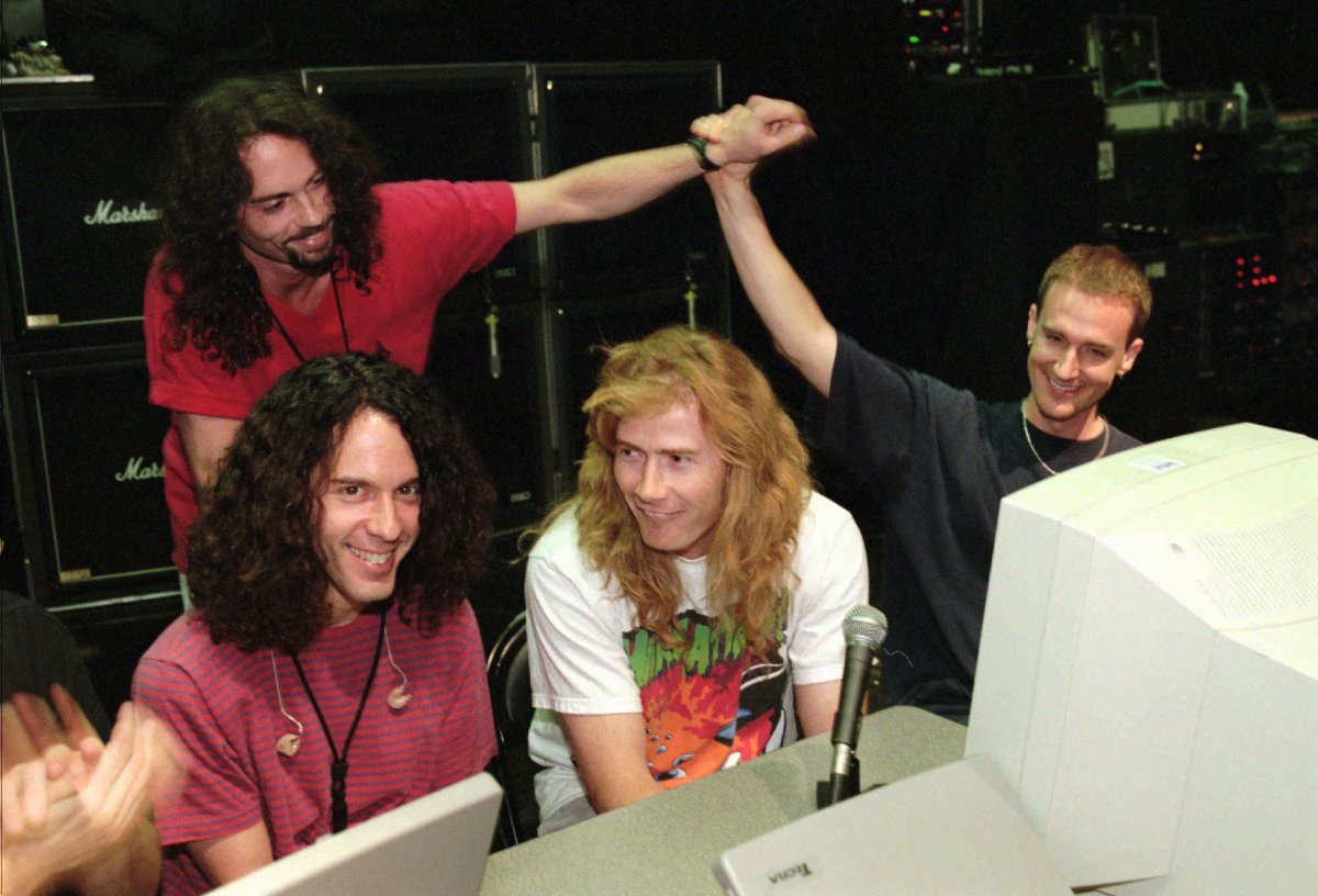 FILE - In this July 24, 1997, file photo, lead guitarist Marty Friedman, left, and lead singer/guitarist Dave Mustaine, center, field questions while bassist David Ellefson, right, high-fives drummer Nick Menza, back left, during a live chat on the internet held at The Joint inside the Hard Rock hotel-casino in Las Vegas. A family spokesman said Menza, former drummer for influential metal band Megadeth, died after collapsing on stage Saturday, May 21, 2016, during a performance of his progressive jazz trio in Southern California. 