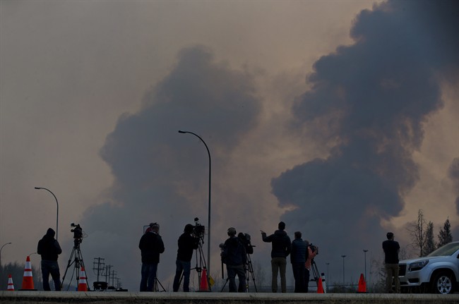 Media watch as smoke billows in the sky near a wildfire in Fort McMurray, Alta., on Friday, May 6, 2016. The Alberta provincial government, which declared a state of emergency, said more than 1,100 firefighters, 145 helicopters, 138 pieces of heavy equipment and 22 air tankers were fighting the fire, but Chad Morrison, Alberta's manager of wildfire prevention, said rain is needed. 