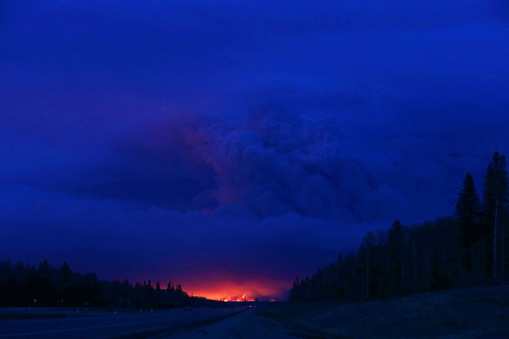 A plume of smoke hangs in the air as forest fires rage on in the distance in Fort McMurray, Alberta on May 4, 2016.