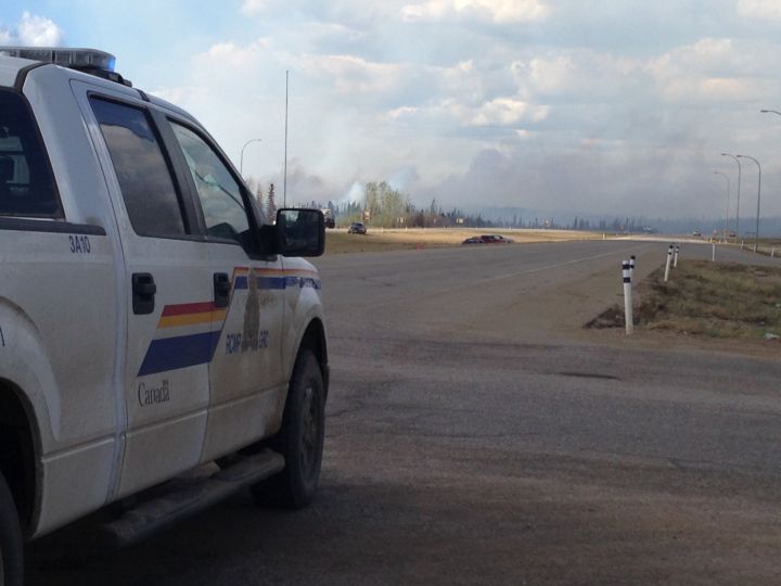 An RCMP vehicle at Highway 63 and Highway 881 south of Fort McMurray looks on as plumes of smoke can be seen in the distance hanging over the city. Sunday, May 8, 2016.