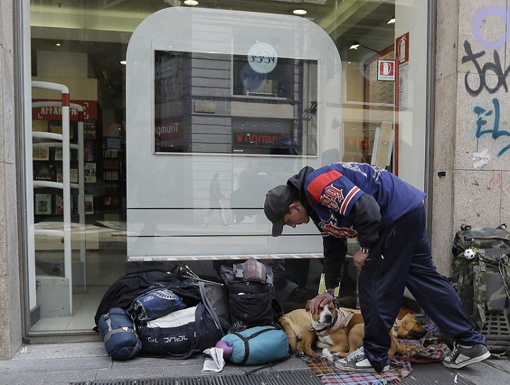 An homeless caresses his dog outside a shop window in Milan, Italy, Saturday, April 6, 2013. Italy's Supreme Court ruled Monday it was not a crime for a homeless man to steal a small amount of food in order to eat. (File photo).