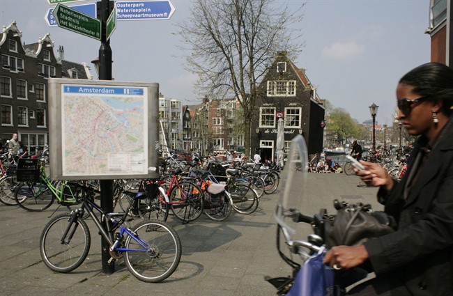 A woman on a bicycle using her cellphone as she rides past a city map in Amsterdam, Netherlands. 