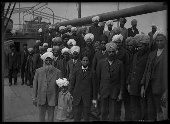 Sikh men and a boy are pictured onboard the Komagata Maru. Businessman Gurdit Singh is seen wearing a light-coloured suit in the left foreground.