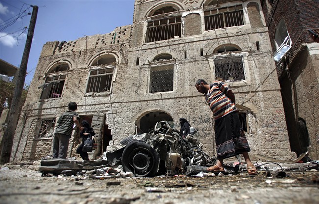 FILE - In this Tuesday, June 30, 2015 file photo, People stand amid wreckage of a vehicle at the site of a car bomb attack near a military hospital in Sanaa, Yemen.