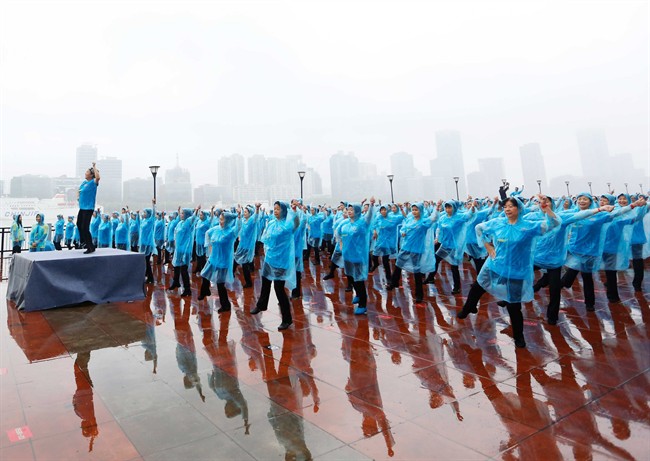 In this Saturday, May 21, 2016 photo, women wearing raincoats dance in unison on the Bund in Shanghai. According to the Guinness World Records website, 31,697 participants in Beijing, Shanghai and four other cities set a new world record on Saturday for mass plaza dancing in multiple locations by performing choreographed dance moves together for more than five minutes. (Chinatopix via AP) .
