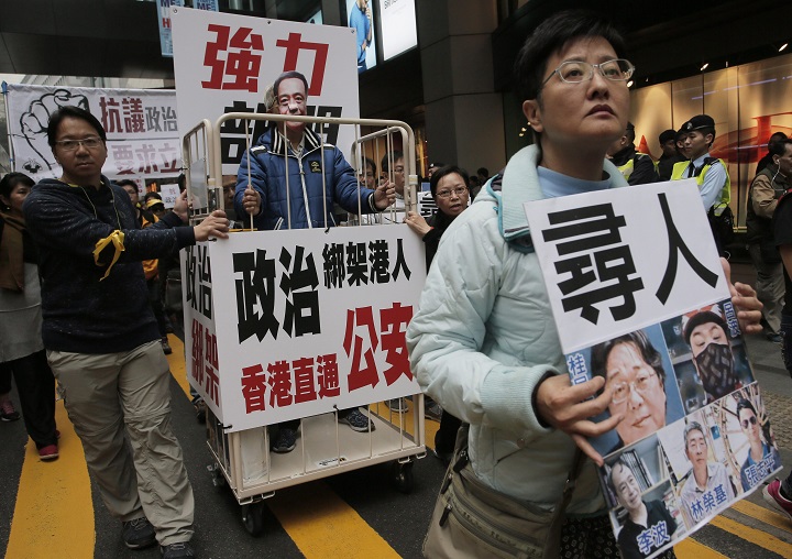 FILE - In this Sunday, Jan. 10, 2016 file photo, led by a man holding a sign that reads "missing men," a protester wearing a mask of missing bookseller Lee Bo stands in a cage during a protest against the disappearances of booksellers in Hong Kong after five men associated with a Hong Kong publisher known for books critical of China's leaders have vanished one by one, alarming activists and deepening suspicions that mainland authorities are squeezing free expression in the enclave.
