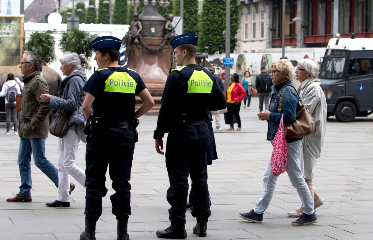People walk by police standing guard outside the Antwerp Central train station in Antwerp, Belgium on Saturday, June 18, 2016. Police and the bomb squad unit responded to a suspect package in the Antwerp station while the Belgian federal prosecutor's office said early Saturday that homes and car ports were searched in 16 municipalities, mostly in and around Brussels in an anti-terror sweep. 