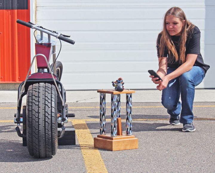 Erica Penner of the Carmangay Outreach team takes a photo of their chopper and the trophy they won in the Biker Build-Off Challenge.