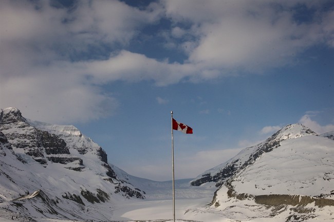 FILE - The Canadian flag flies over the Columbia Icefields' Athabasca Glacier in Jasper National Park, in a May 7, 2014, file photo. Parks Canada is preparing to go to the public with plans for a $66-million, 107-kilometre bike trail from Jasper, Alta., to the Columbia Icefields along the Jasper-Banff highway, one of the country's most scenic drives.