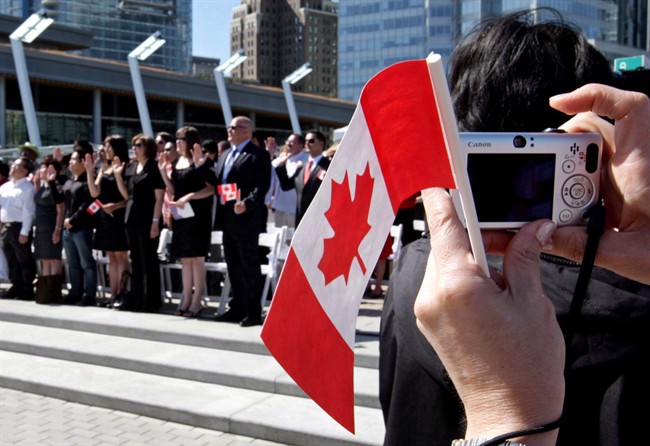 A woman takes a photograph while holding a Canadian flag during a citizenship ceremony in Vancouver, B.C., on July 1, 2009.