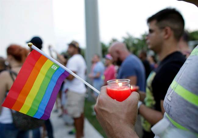 A man holds a candle and a rainbow flag during a vigil in memory of the victims of the Orlando mass shooting.