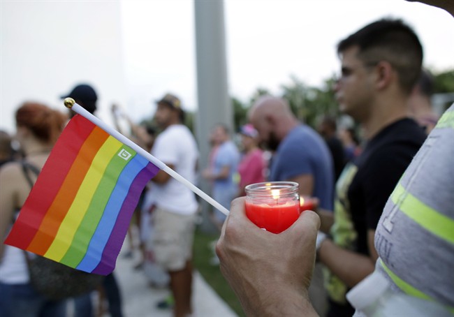 A man holds a candle and a rainbow flag during a vigil in memory of the victims of the Orlando mass shooting.