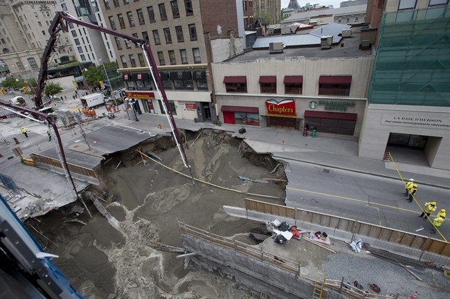 Workers look on as boom concrete pumps fill a large sinkhole that formed Wednesday morning on Rideau Street, Thursday, June 9, 2016 in Ottawa.