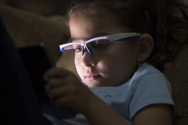 Liliya Sahiholnasab, 6, uses a special pair of glasses to help her correct her posture when using a tablet at her home in Richmond, B.C., Wednesday, June, 22, 2016. Dr. Vahid Sahiholnasab has designed a pair of high-tech glasses to prevent children from developing bad posture while playing with devices like smartphones and video games.